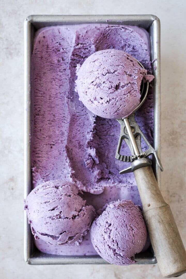 Blueberry ice cream being scooped out of a metal pan.