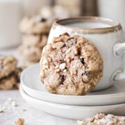 A cranberry almond oatmeal cookie, resting against a coffee cup.