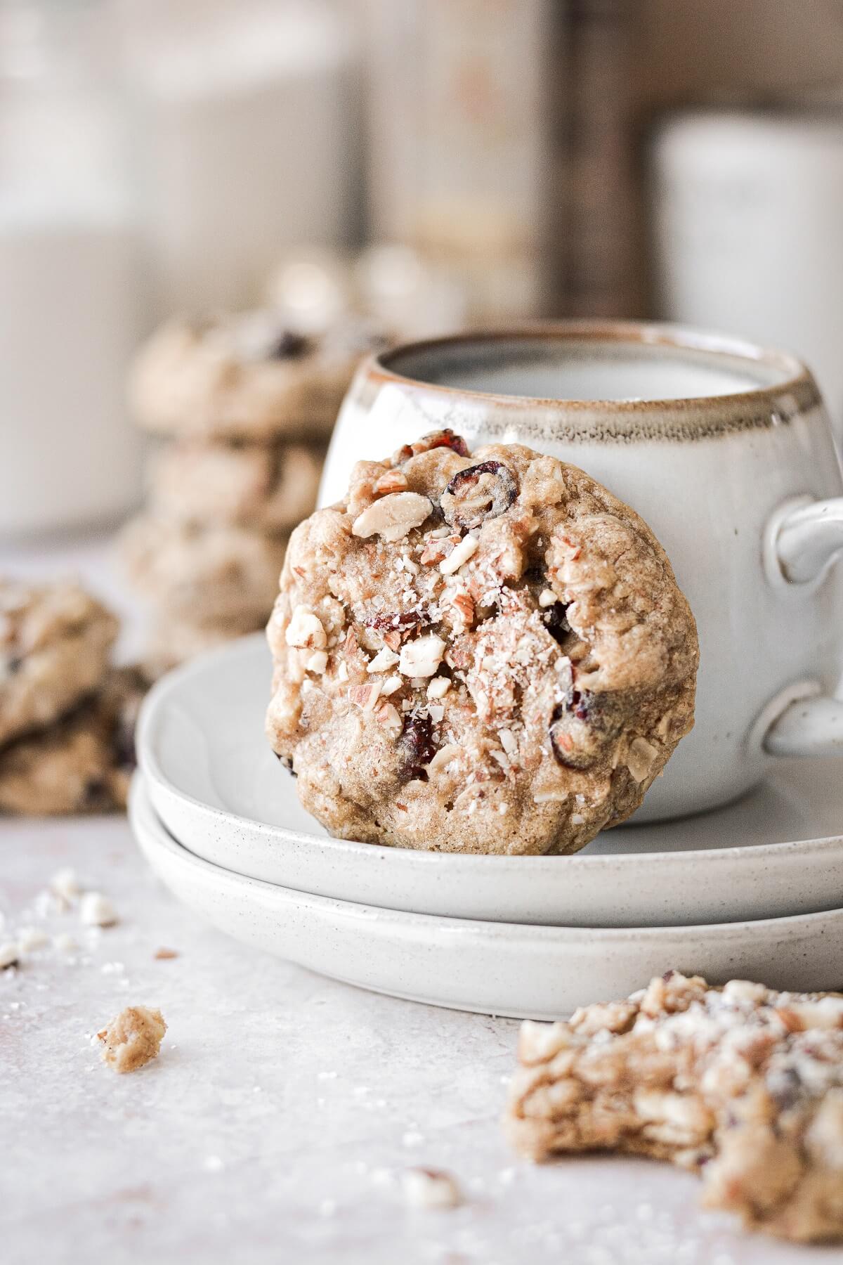A cranberry almond oatmeal cookie, resting against a coffee cup.