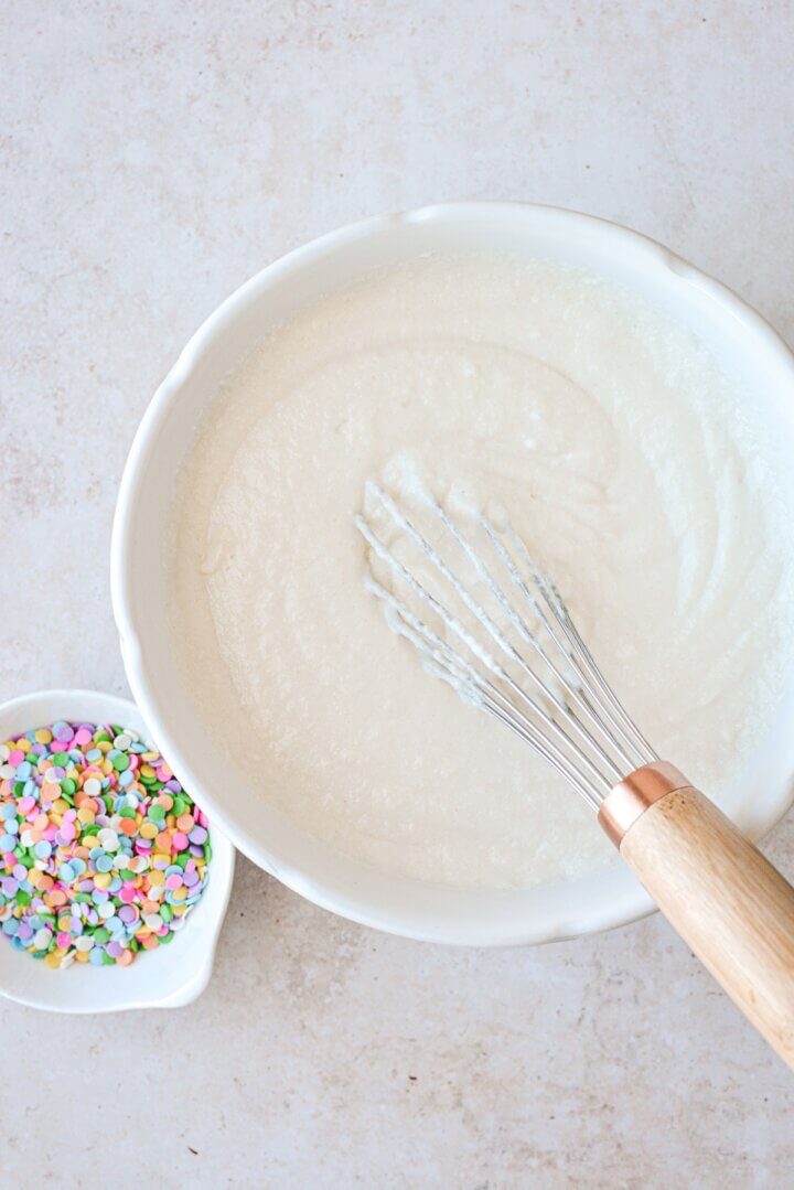 Vanilla cake batter next to a bowl of sprinkles.