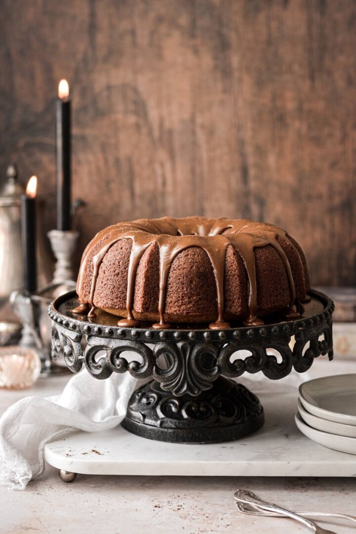 Pumpkin bundt cake with espresso icing dripping down, on a black cake stand.