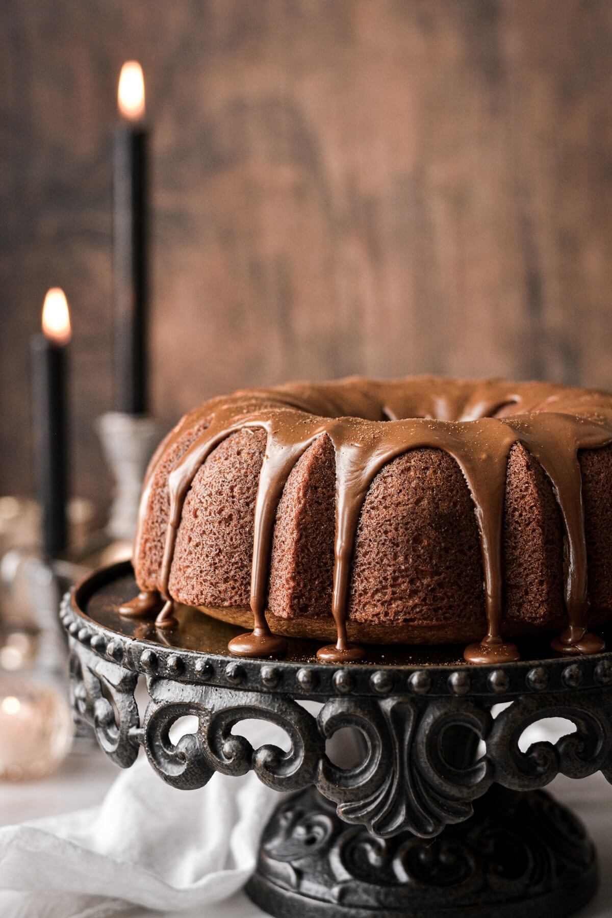 Pumpkin bundt cake with espresso icing dripping down, on a black cake stand.
