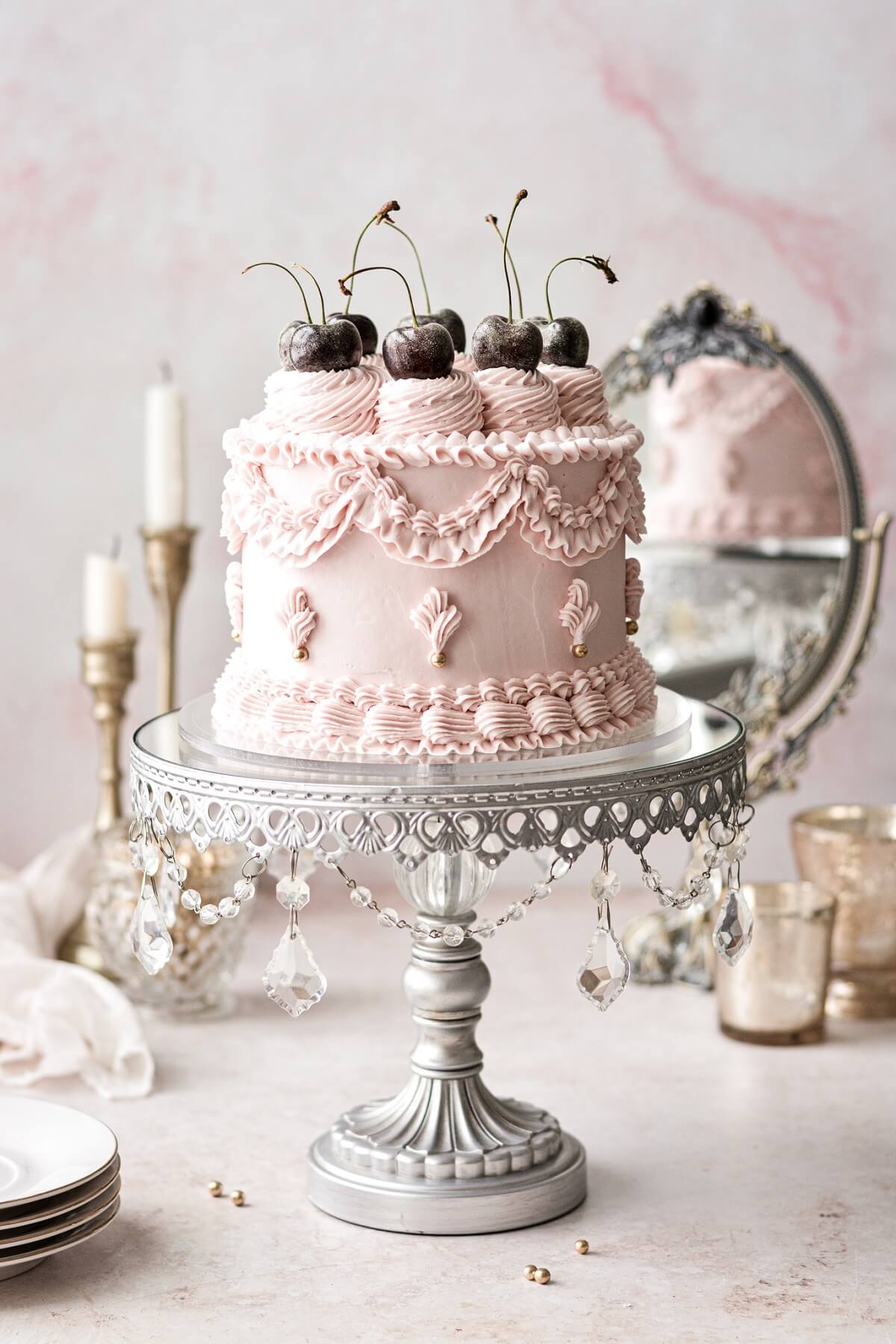 Pink chocolate cherry lambeth cake on a silver cake stand.