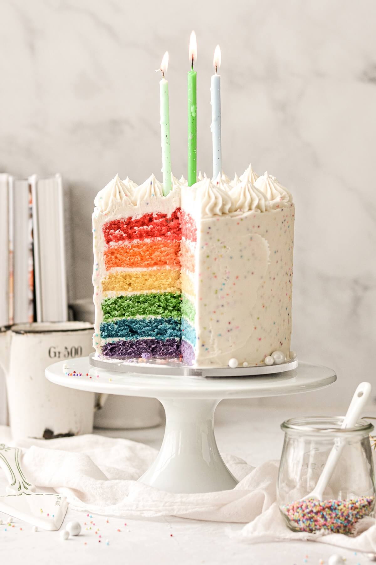 Rainbow birthday cake with sprinkles and candles.