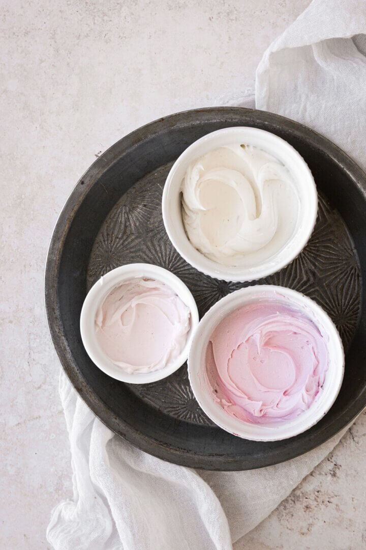 Three bowls of buttercream in different shades of pink and white.