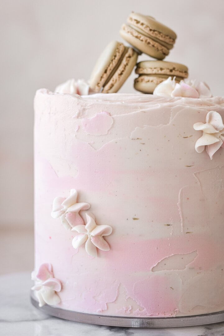 A cake with textured watercolor buttercream, piped flowers and macarons.