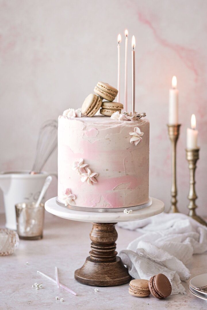 A textured watercolor buttercream cake with candles, macarons and piped flowers.