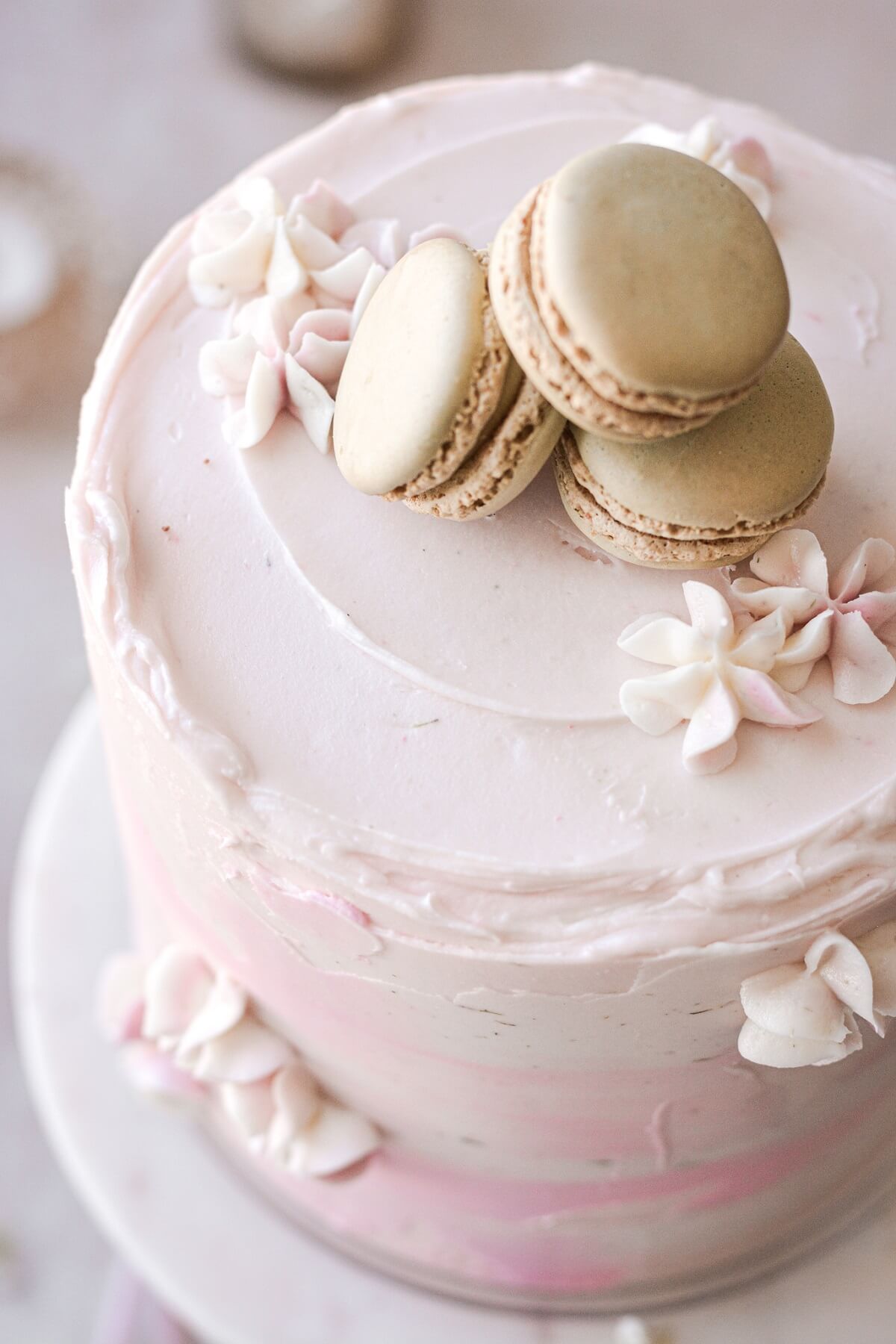 Macarons and piped flowers on a pink watercolor cake.