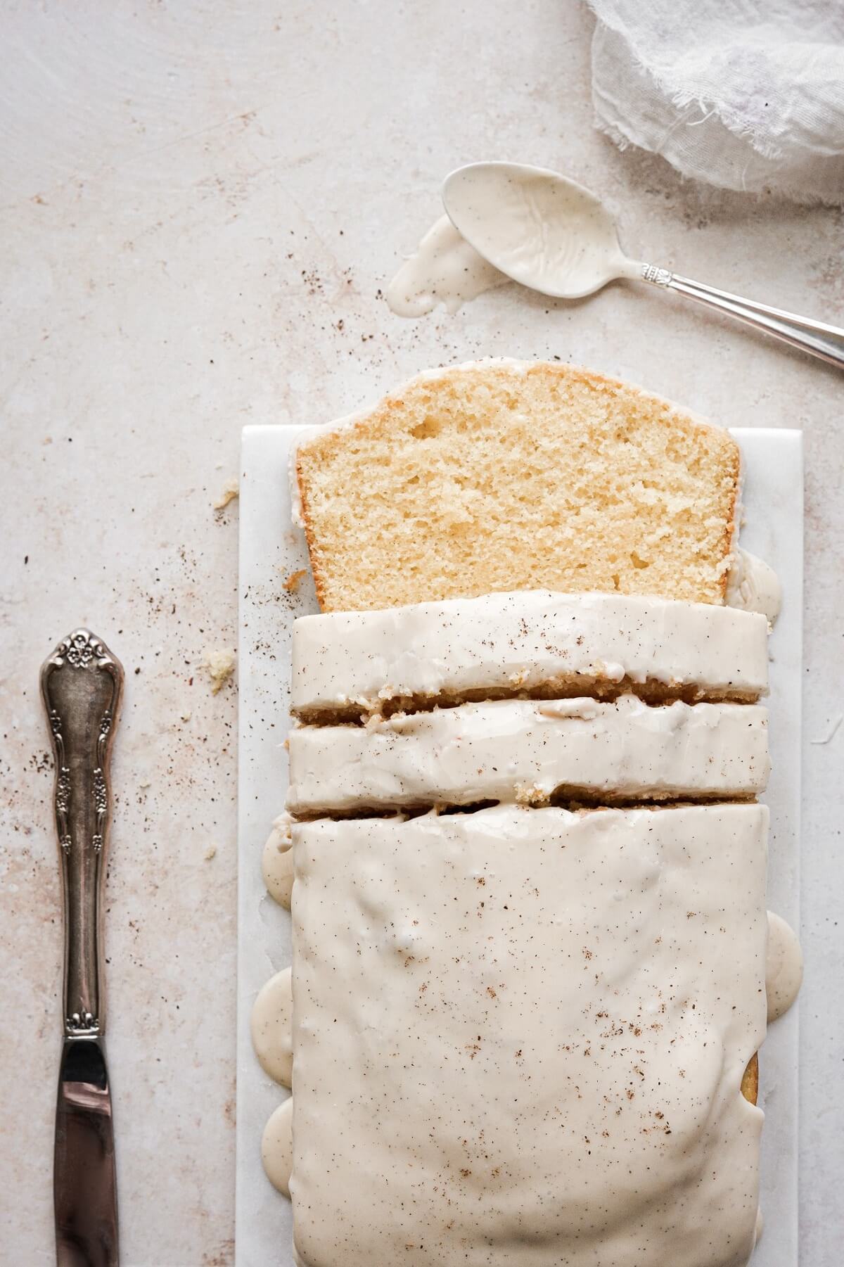 Vanilla loaf cake with vanilla bean icing, with several slices cut.