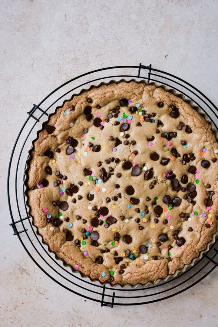 A big chocolate chip cookie birthday cake on a cooling rack.