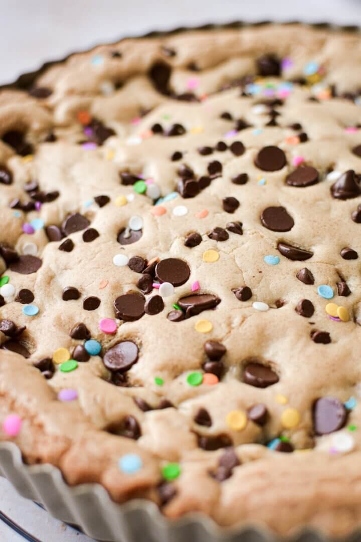 Chocolate chips and confetti sprinkles on a big chocolate chip cookie cake.