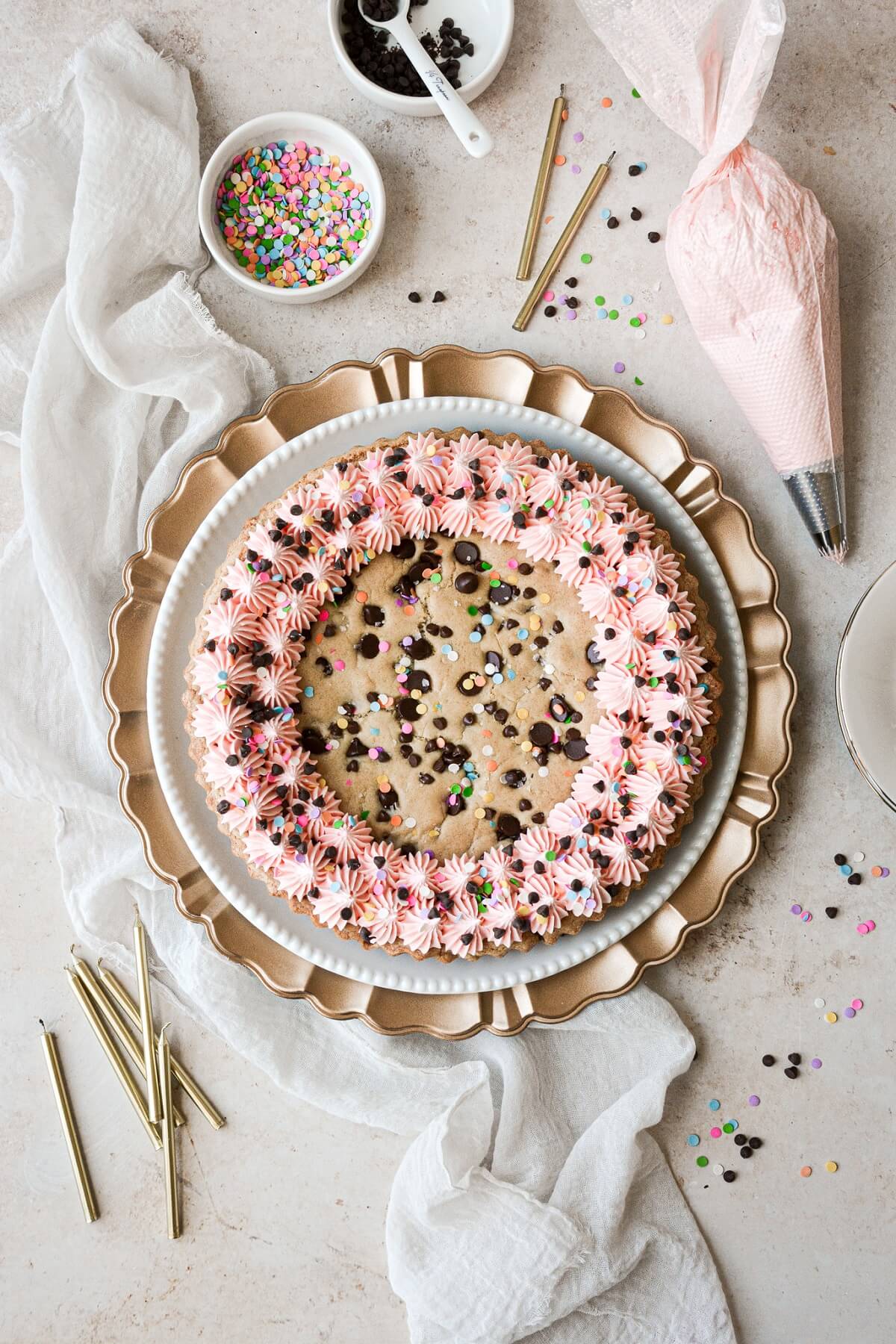 A big chocolate chip cookie birthday cake with pink frosting and sprinkles.