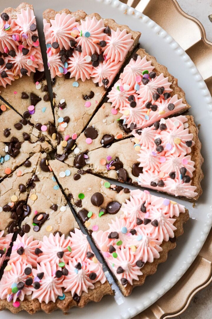 A chocolate chip cookie cake with pink frosting and sprinkles.