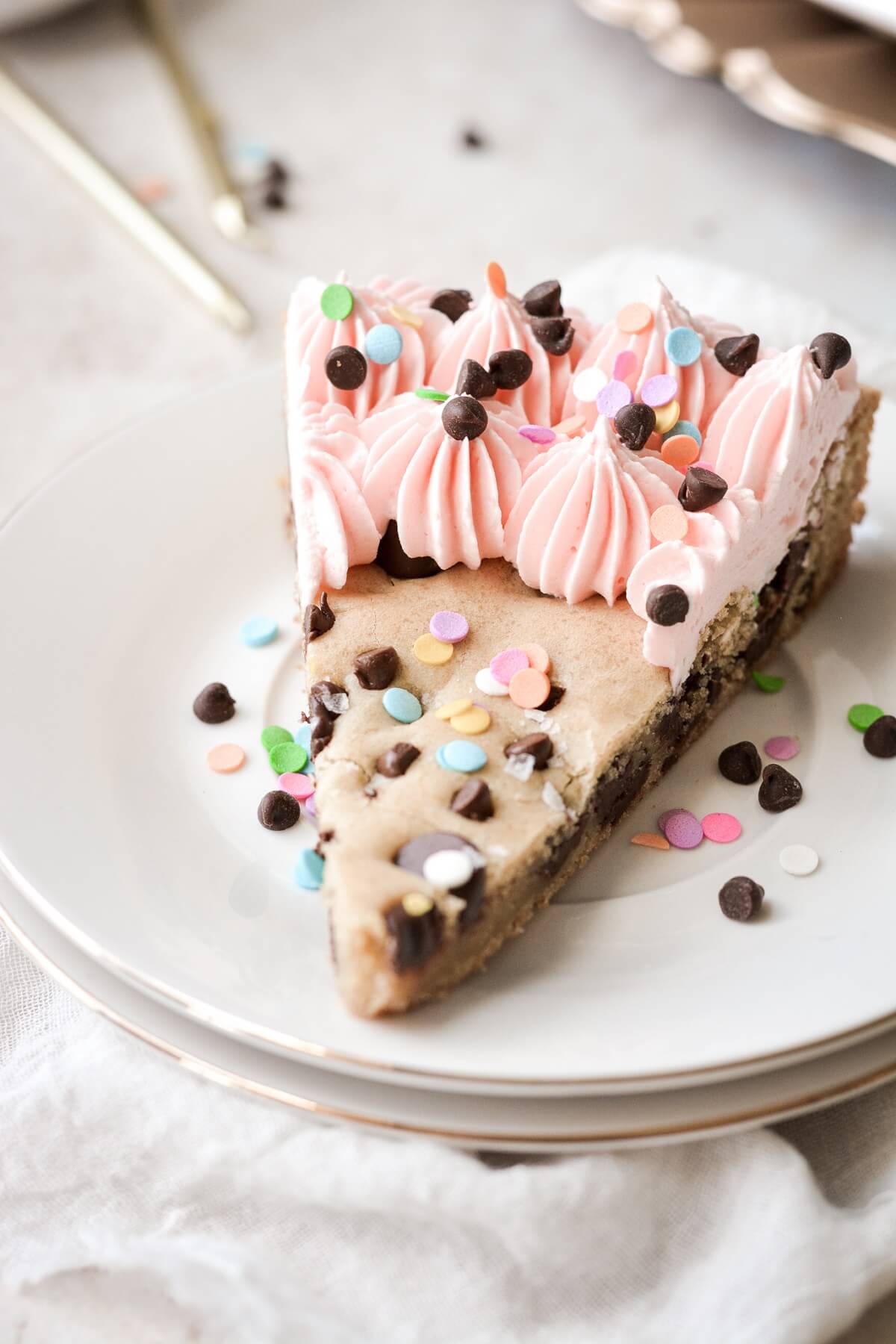 A piece of chocolate chip cookie birthday cake with pink frosting and sprinkles.