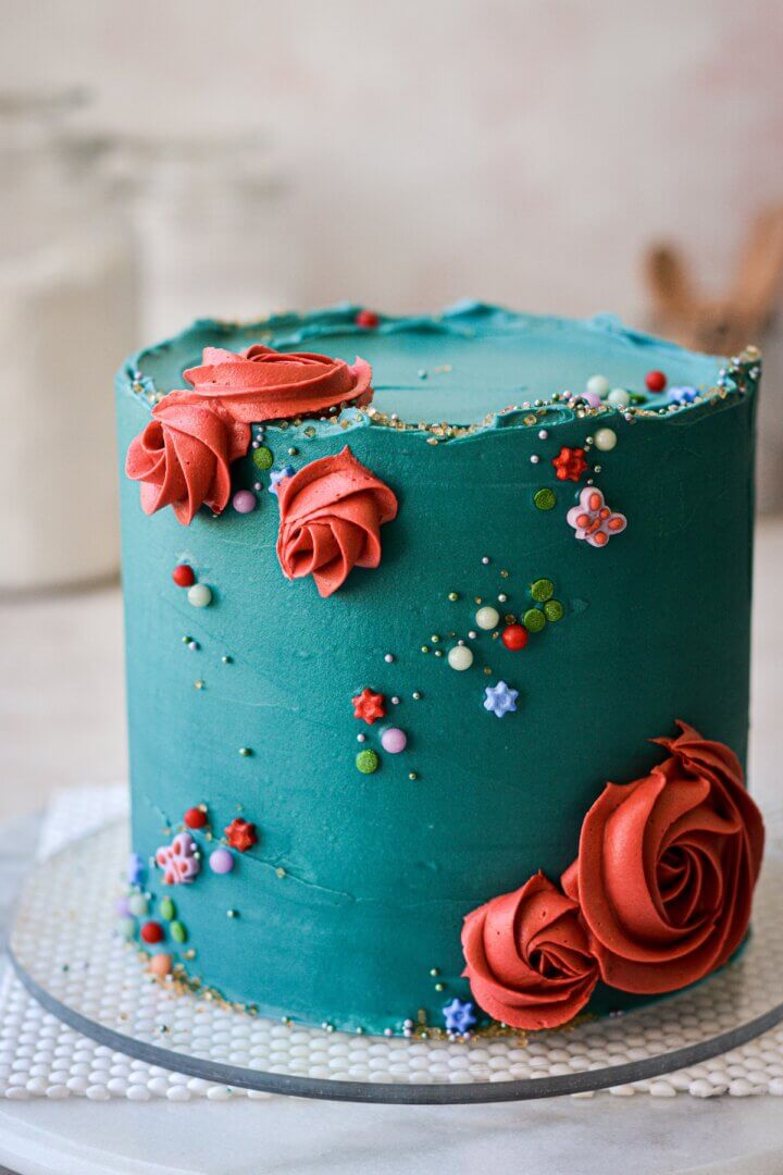 Turquoise cake with sprinkles and red piped flowers.
