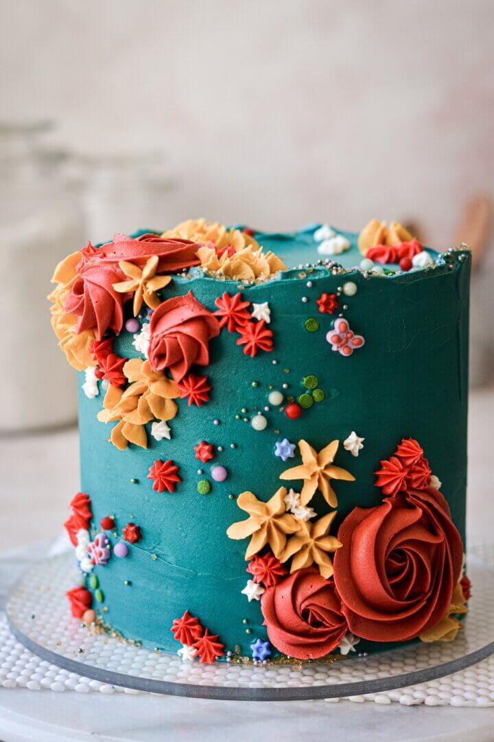 Turquoise cake with sprinkles and red, yellow and white piped flowers.