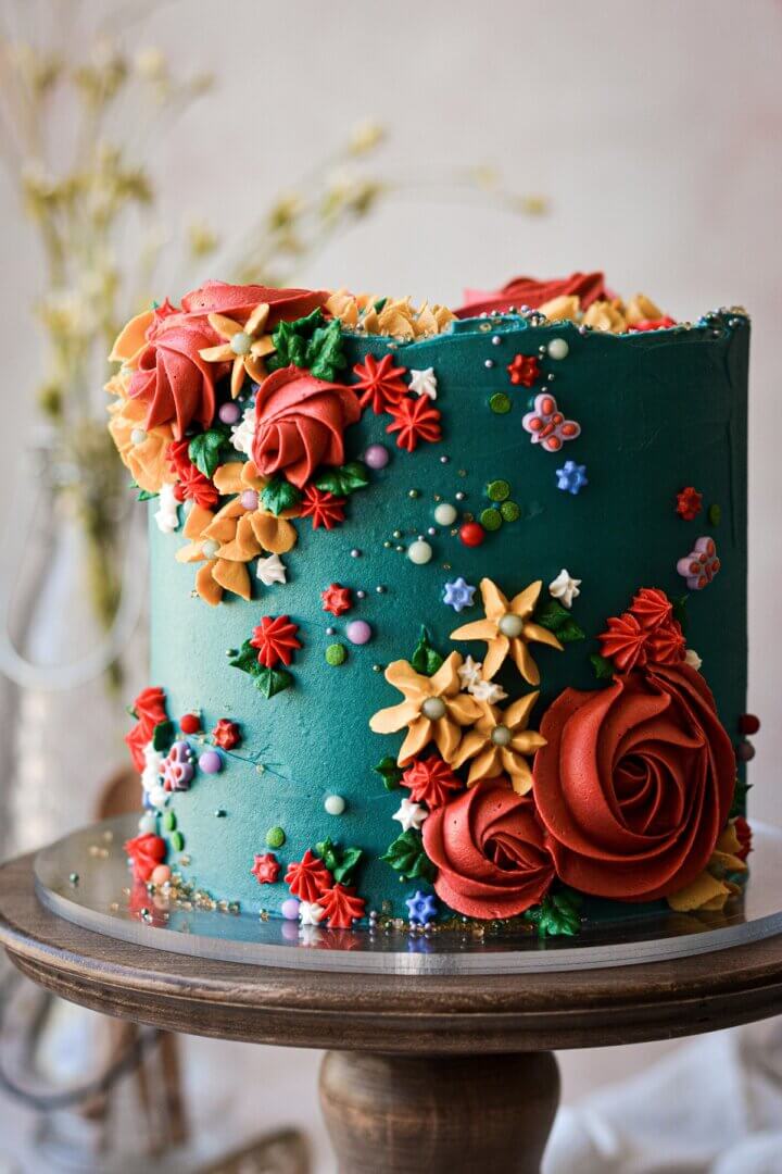 Turquoise floral cake with red and yellow piped buttercream flowers and sprinkles.