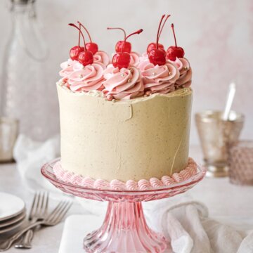 Cherry pistachio layer cake topped with swirls of pink buttercream and maraschino cherries.