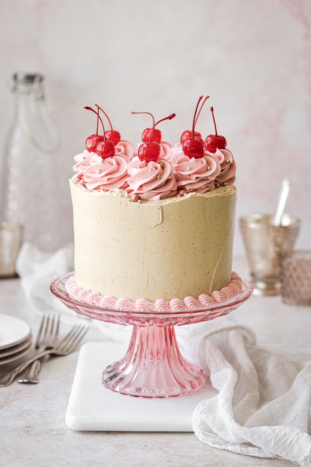 Cherry pistachio layer cake topped with swirls of pink buttercream and maraschino cherries.