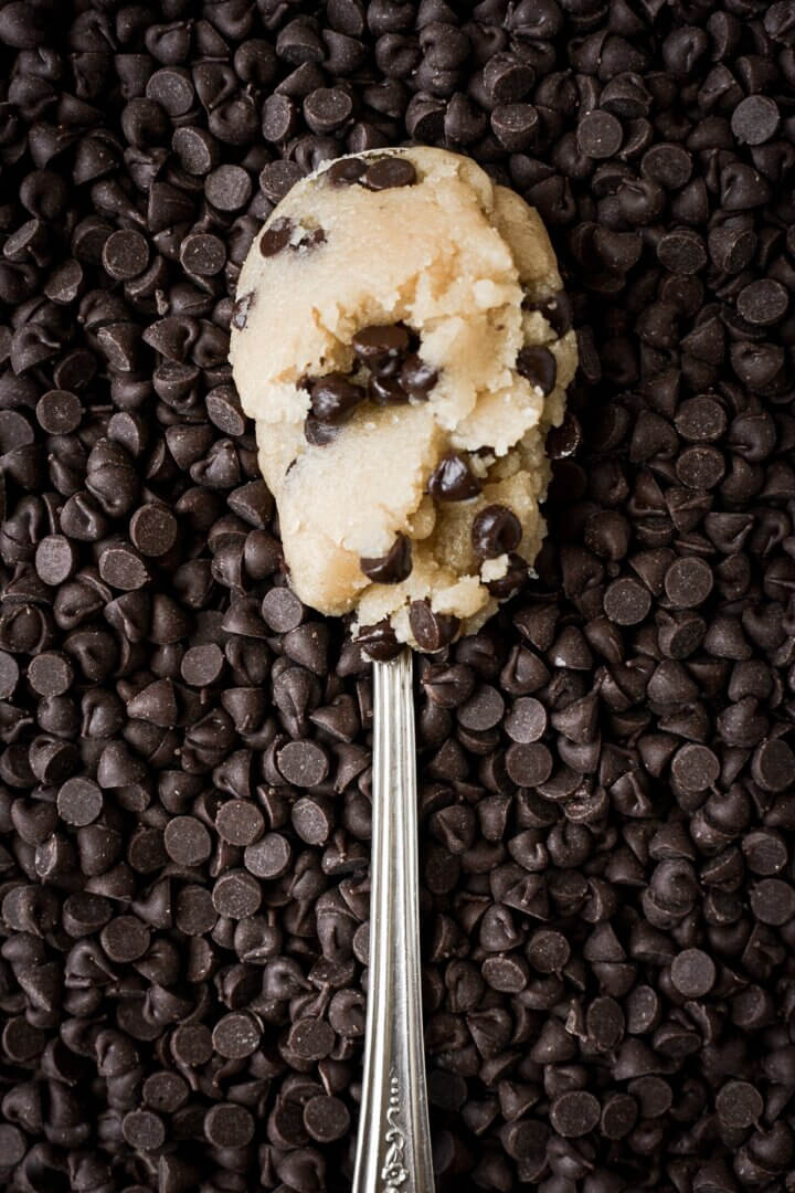 Spoonful of chocolate chip cookie dough resting on chocolate chips.