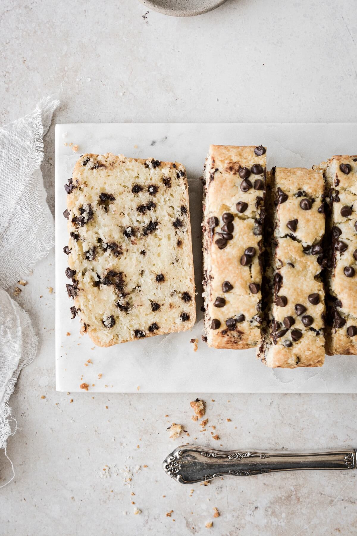 Slices of chocolate chip sour cream loaf cake on a white marble board.