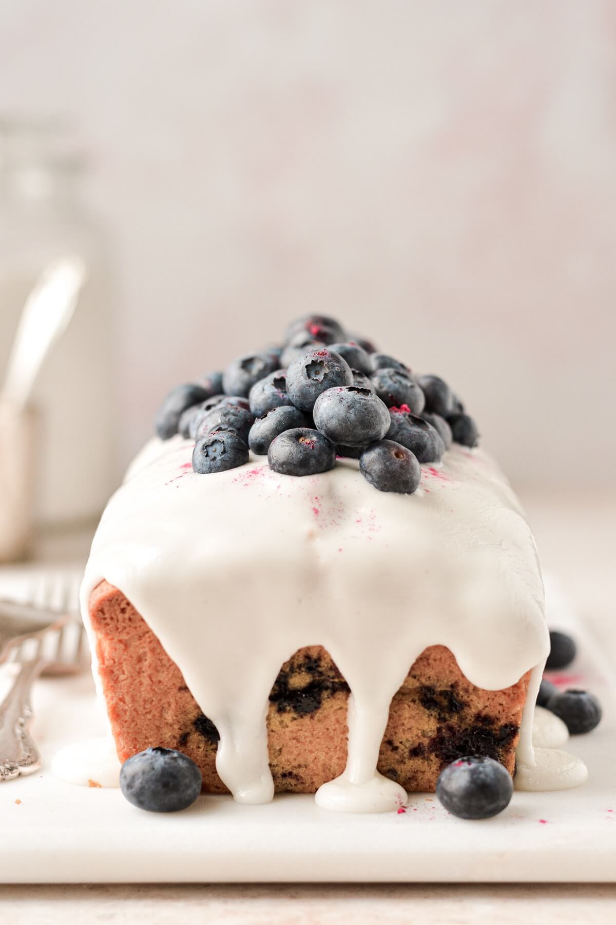 Lemon icing dripping down a lemon blueberry loaf cake.