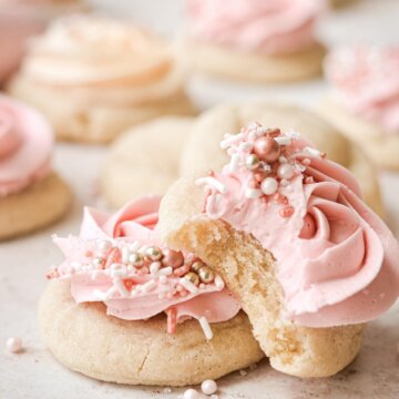 Soft sugar cookies with frosting and sprinkles, one with a bite taken.