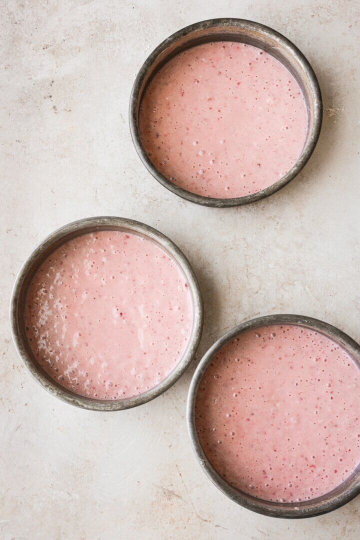 Three cake pans filled with strawberry cake batter.