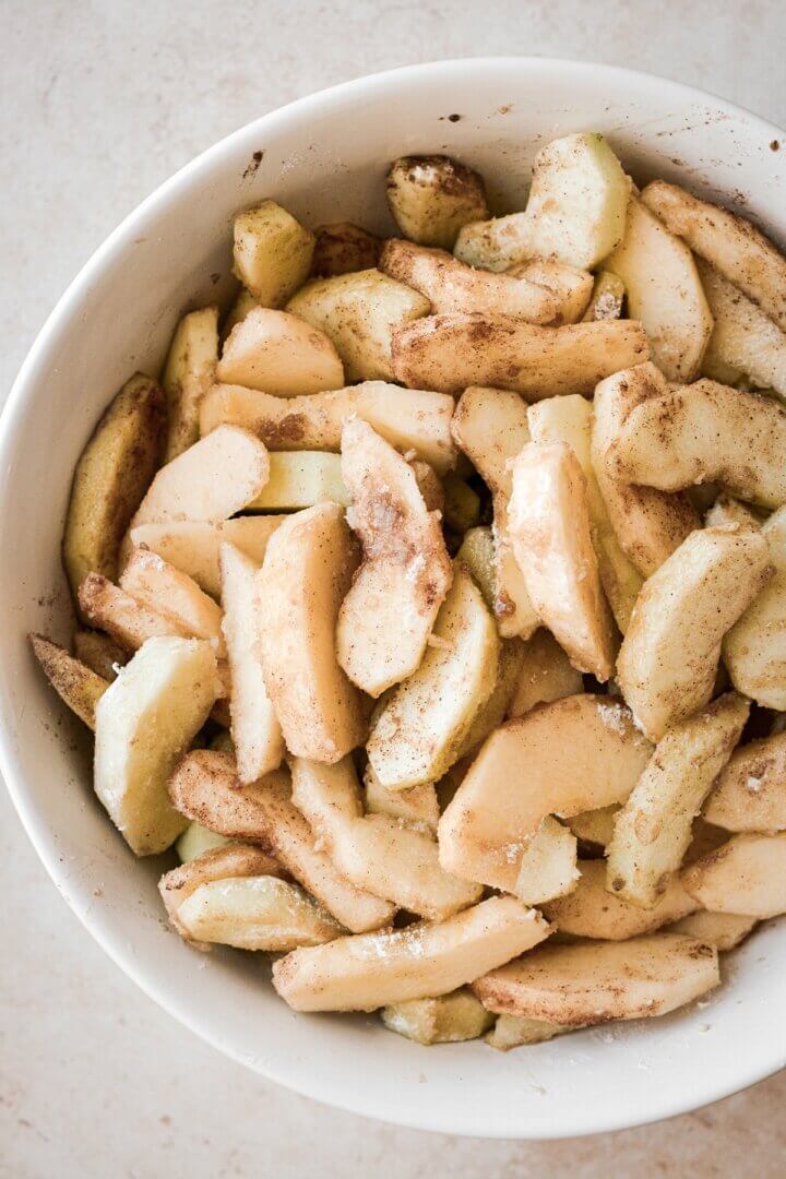 Bowl of sliced apples tossed with sugar and spices.