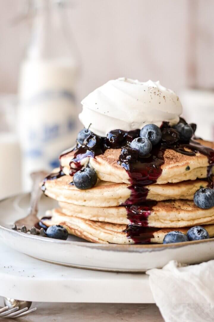 Stack of blueberry pancakes with blueberry sauce and whipped cream.