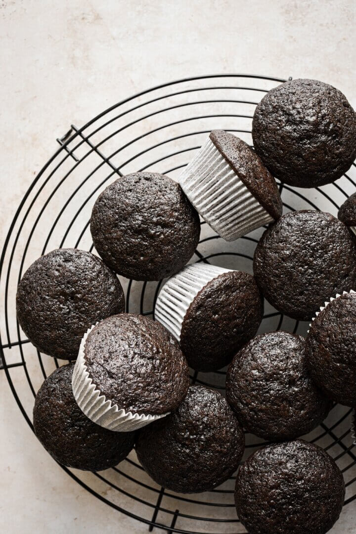 Unfrosted chocolate cupcakes on a black cooling rack.