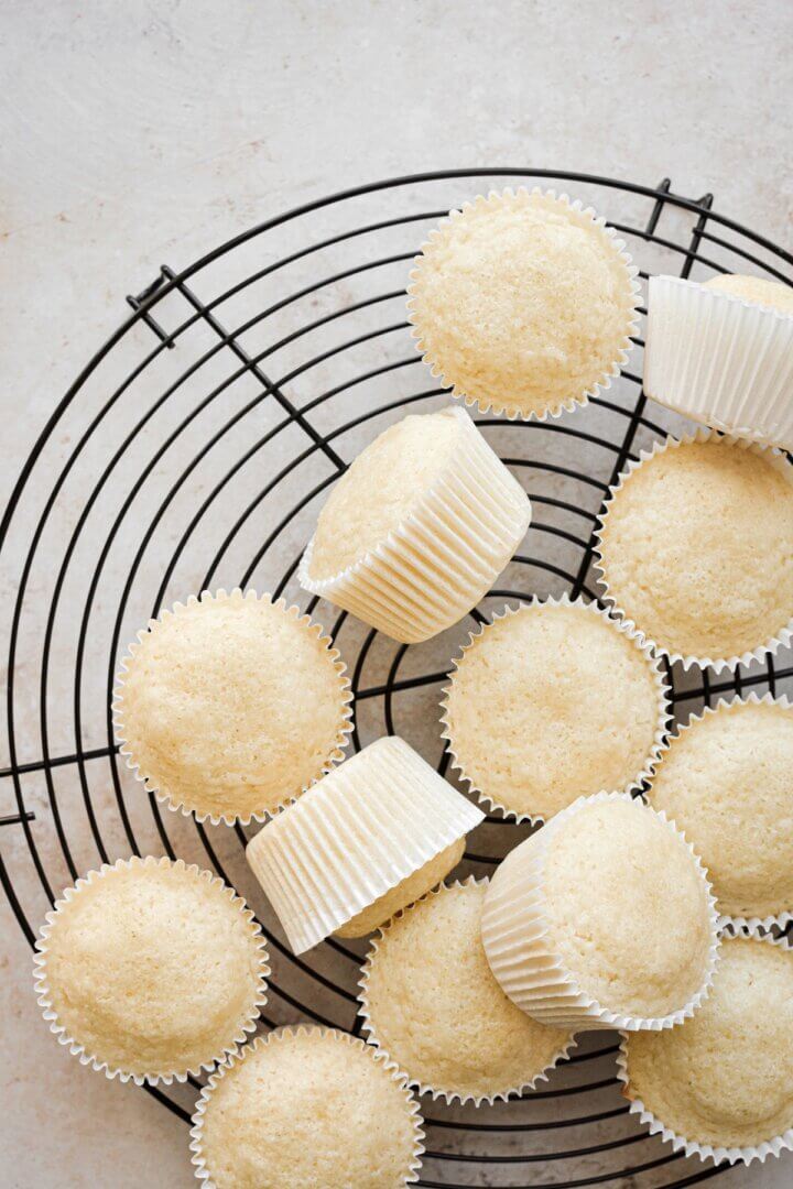 Vanilla cupcakes on a black cooling rack.