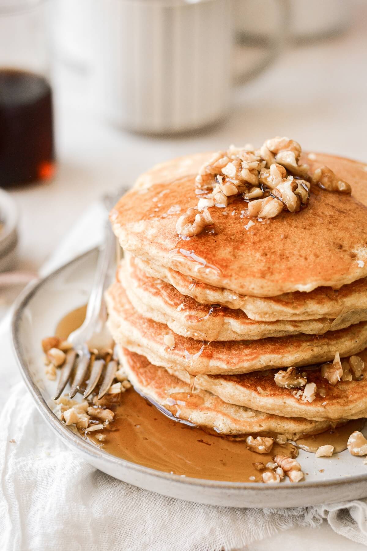 Stack of cornmeal pancakes with syrup and walnuts.