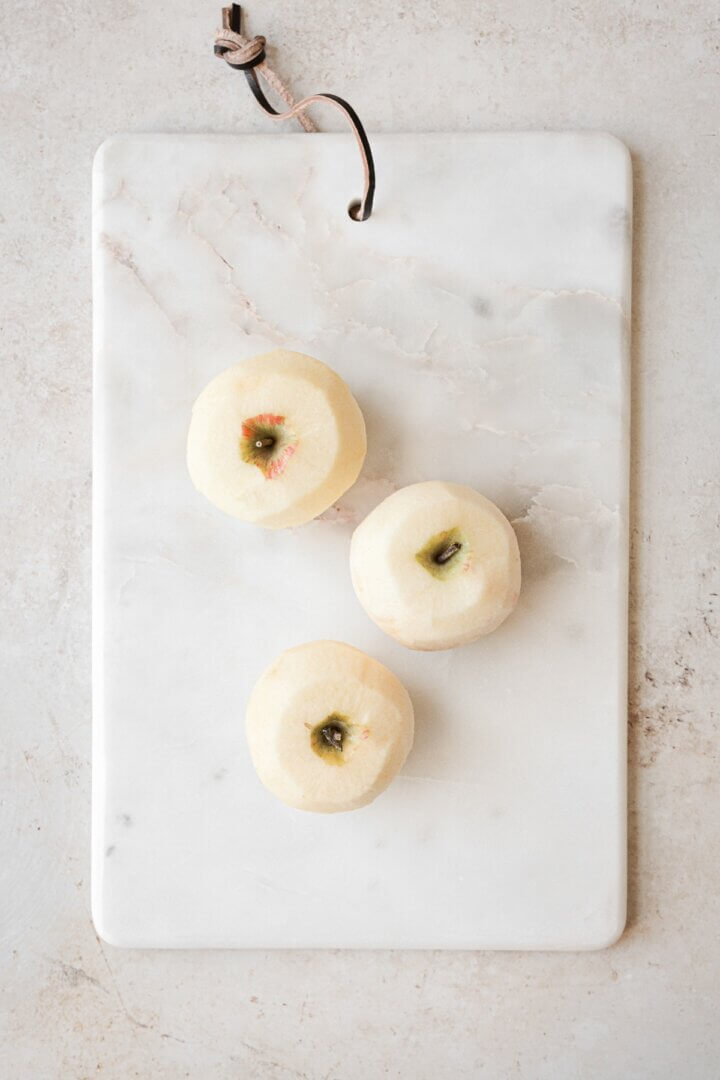 Three peeled apples on a marble board.
