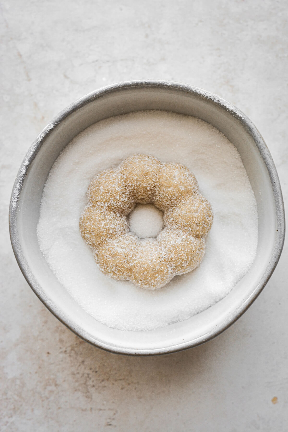 Maple donut in a bowl of sugar.