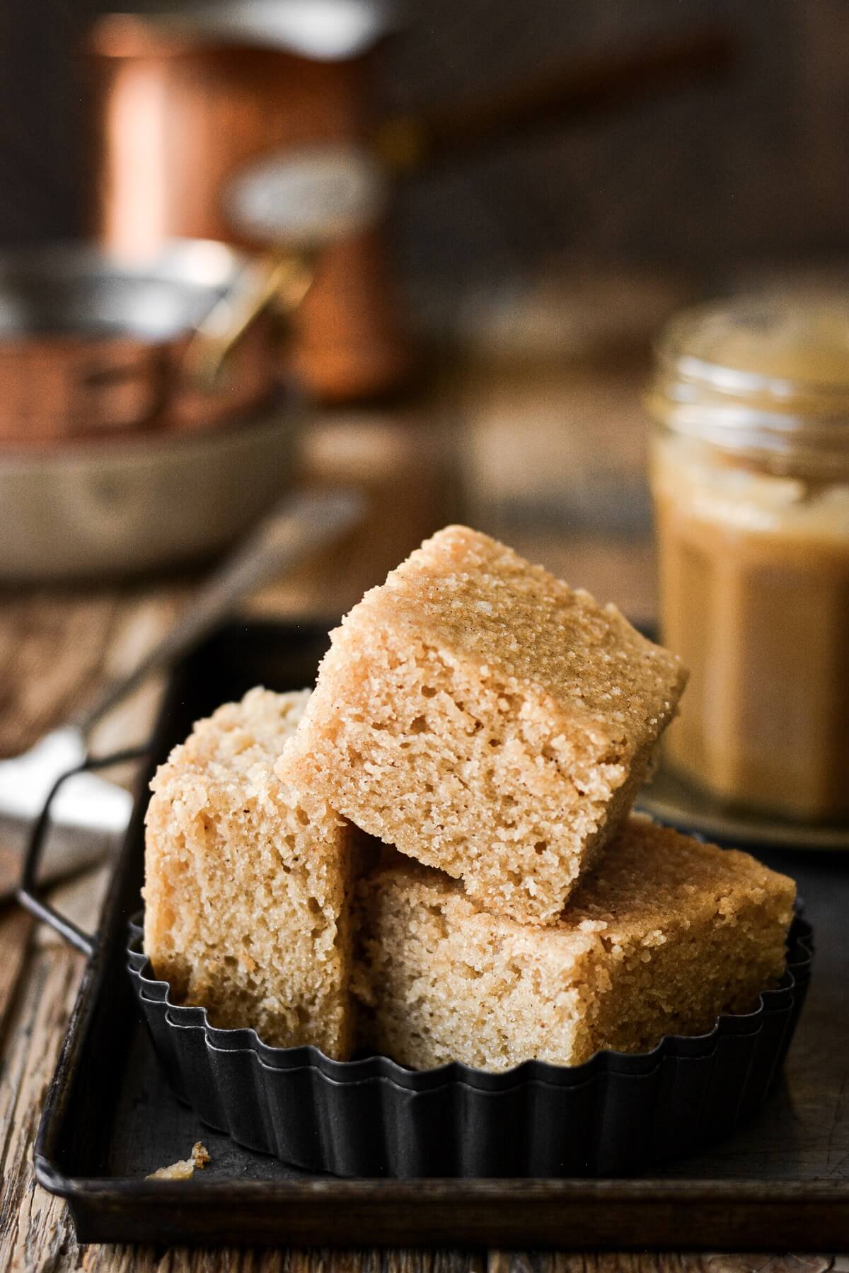 Squares of brown butter cake stacked on a plate next to a jar of toffee.