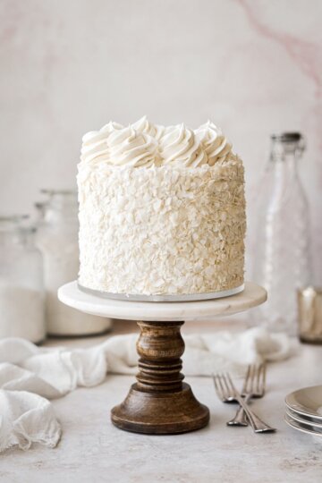 Coconut cake on a marble and wood cake stand.