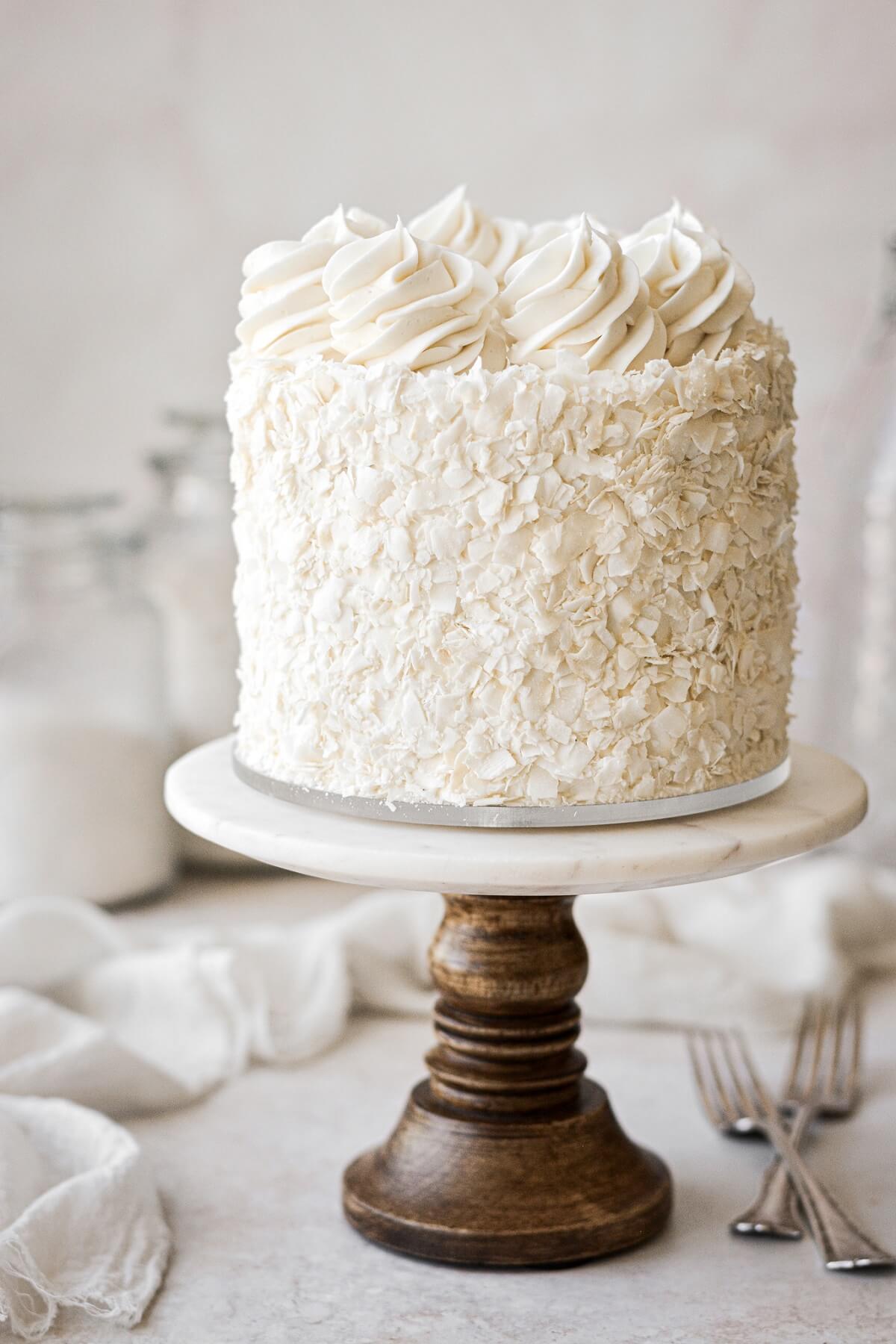 Coconut cake covered in coconut on a marble and wood cake stand.
