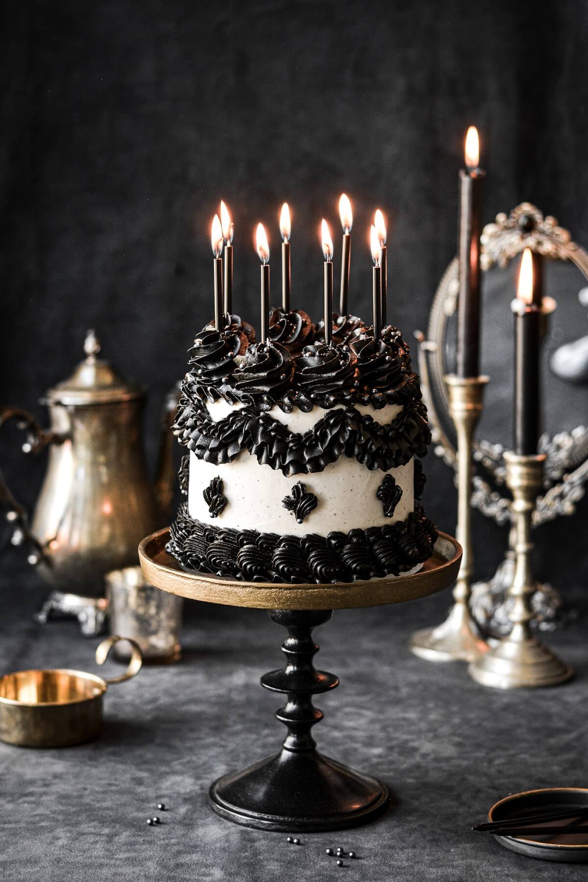 A gothic scene with a black and white Lambeth style cake topped with candles.