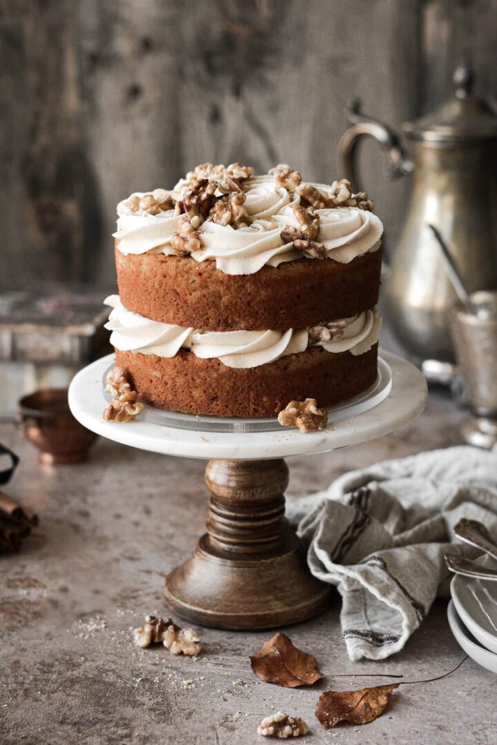 Naked maple walnut cake on a white and marble cake stand.