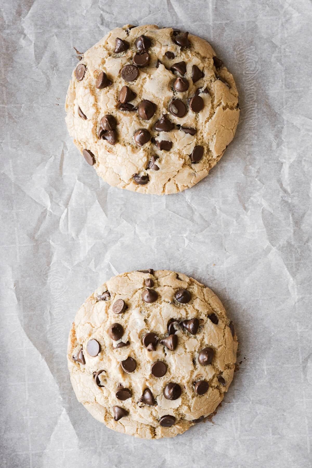 Two big chocolate chip cookies on parchment paper.