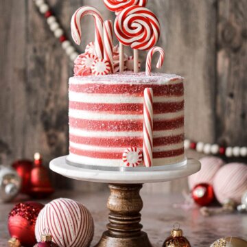 Candy cane cake with red and white striped buttercream and decorated with candy canes and peppermints.