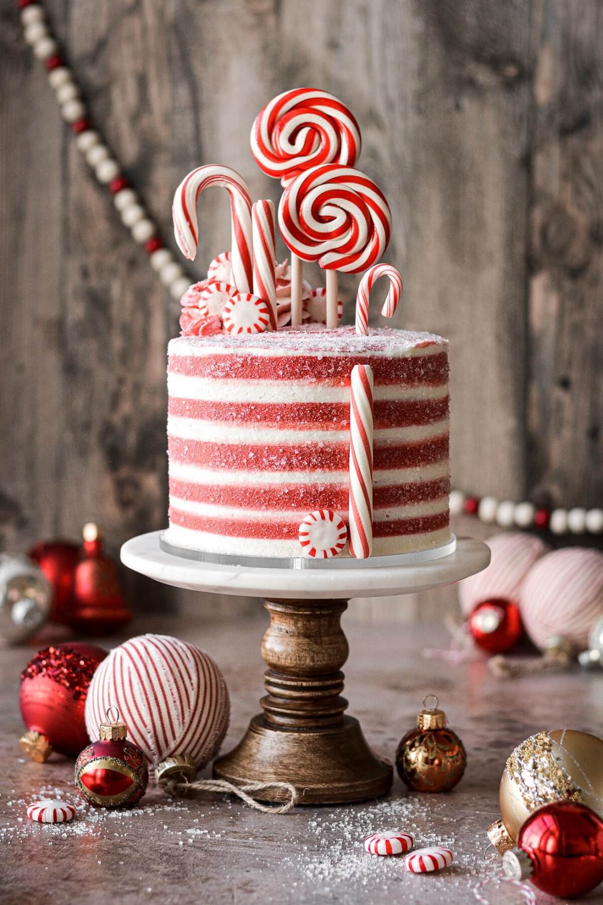 Candy cane cake with red and white striped buttercream and decorated with candy canes and peppermints.