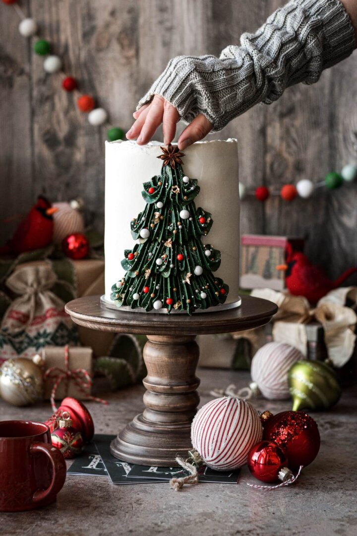 Buttercream Christmas tree cake with a star anise being placed on top.