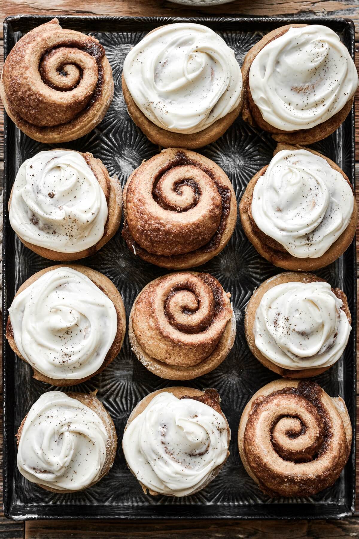 Gingerbread cinnamon rolls with cream cheese frosting on a baking sheet.