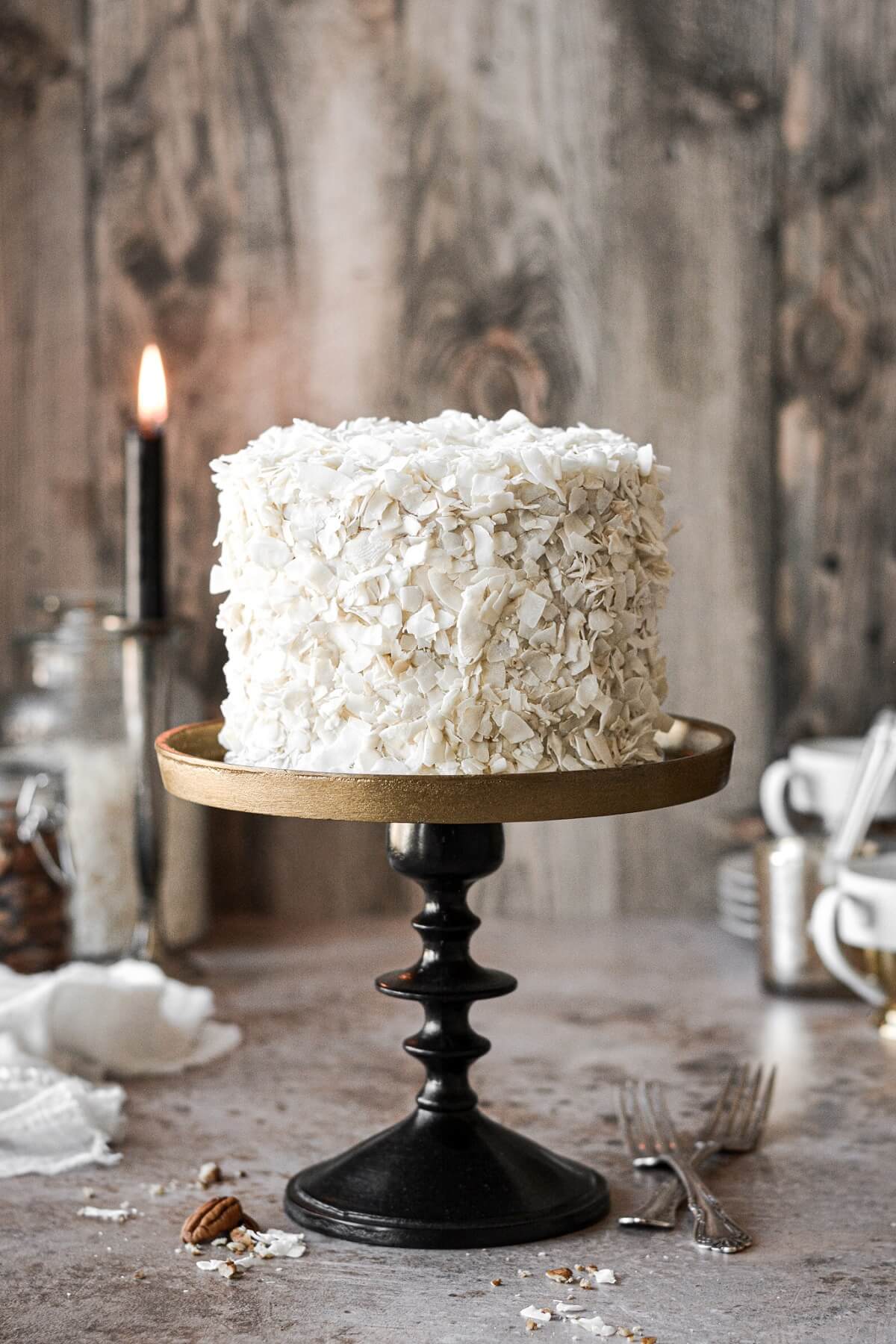 Italian cream cake covered in coconut on a black and bronze cake stand.