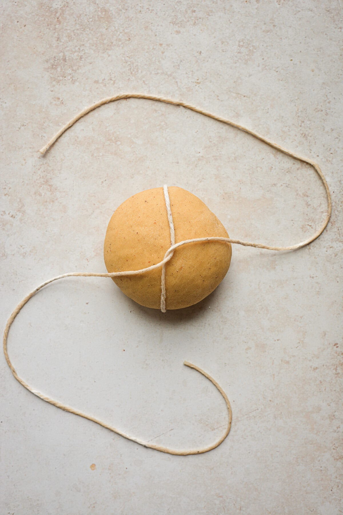 Step 2 for tying pumpkin shaped dinner rolls with twine.
