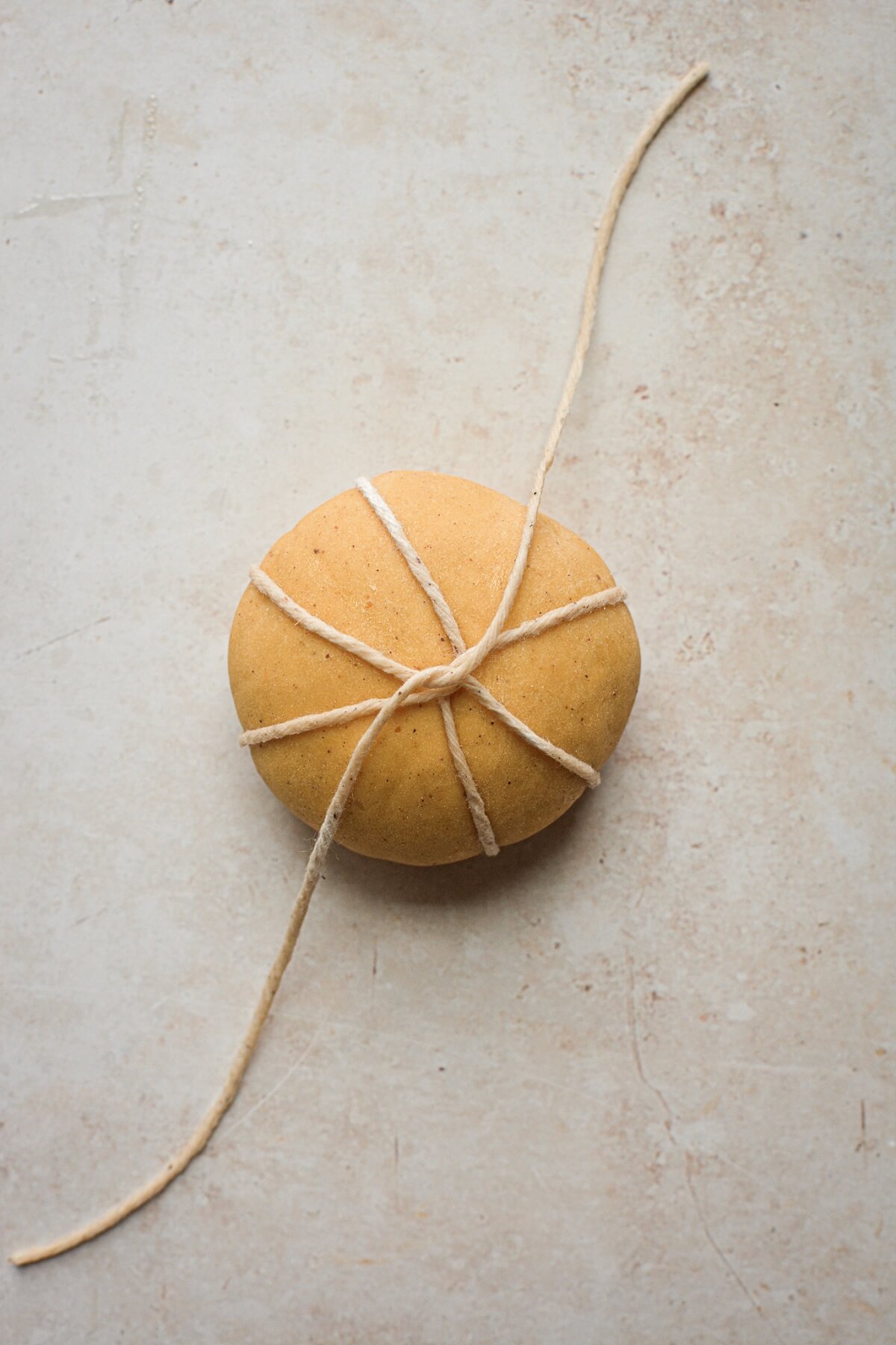 Step 4 for tying pumpkin shaped dinner rolls with twine.
