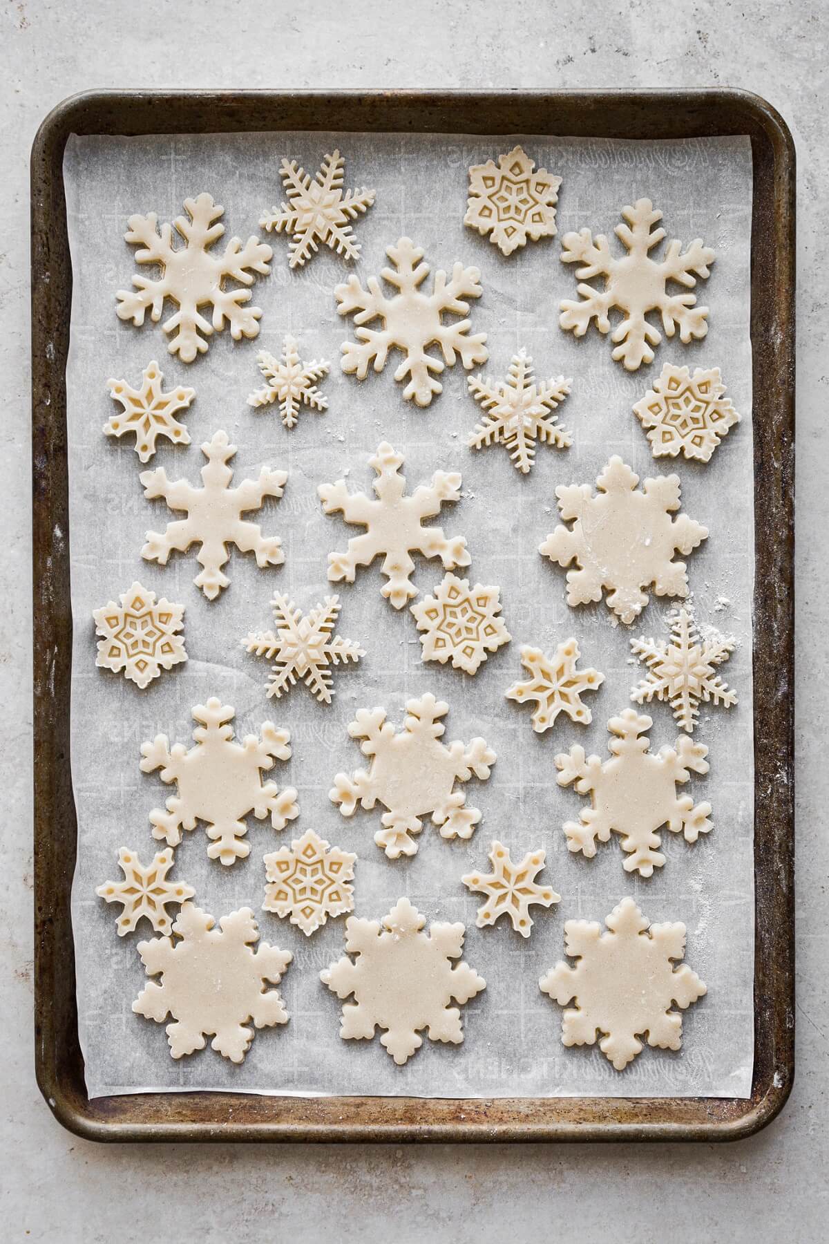 Unbaked snowflake cookies on a baking sheet.