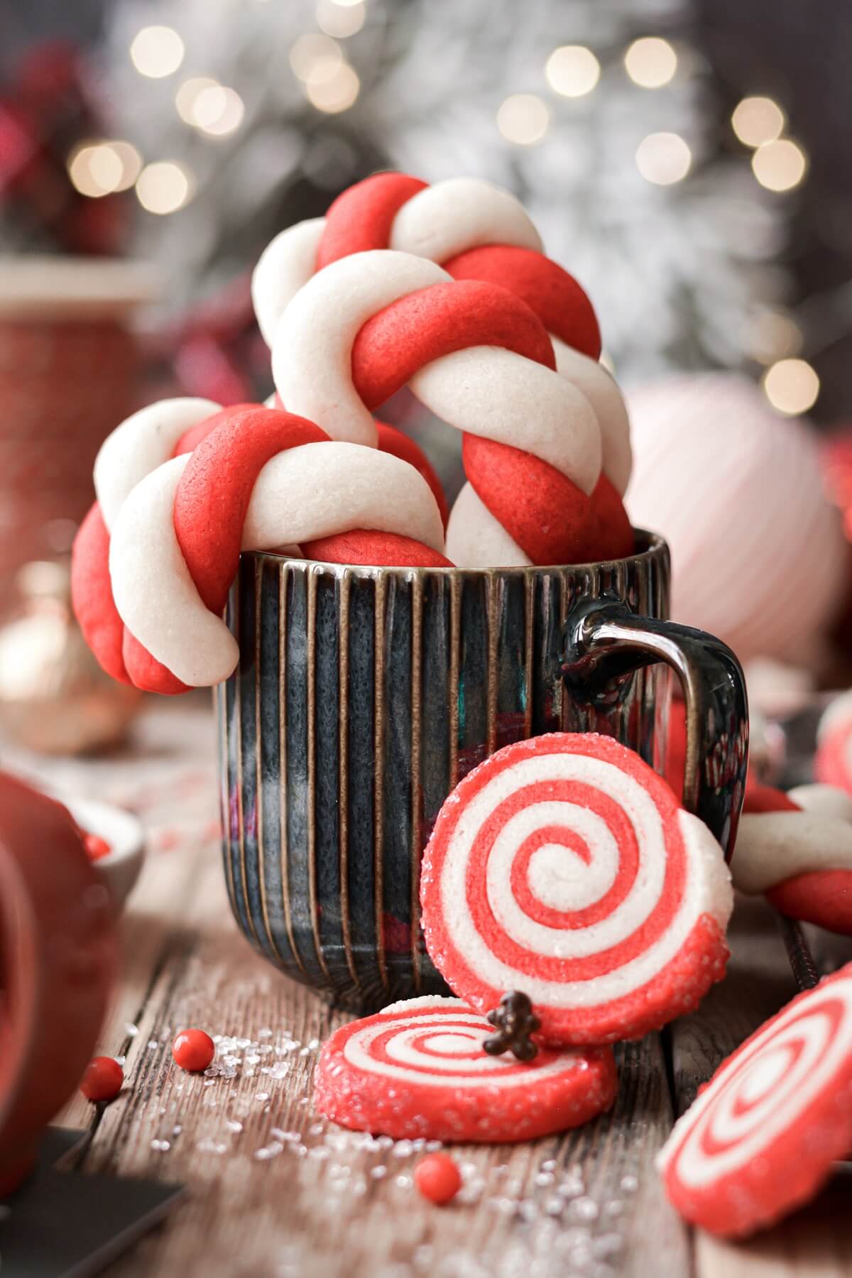 Red and white pinwheel cookies leaning against a coffee mug filled with candy cane cookies.